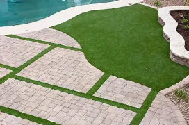 Artificial turf installed next to a pool and in between the stones of the patio.