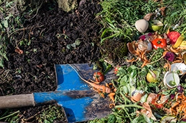 The inside of a compost bin with soil and vegetables and a shovel.