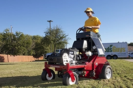 The Grounds Guys service professional operating a stand-up aerator on a lawn.