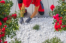 The Grounds Guys service professional installing white pebbles in a front yard garden bed.