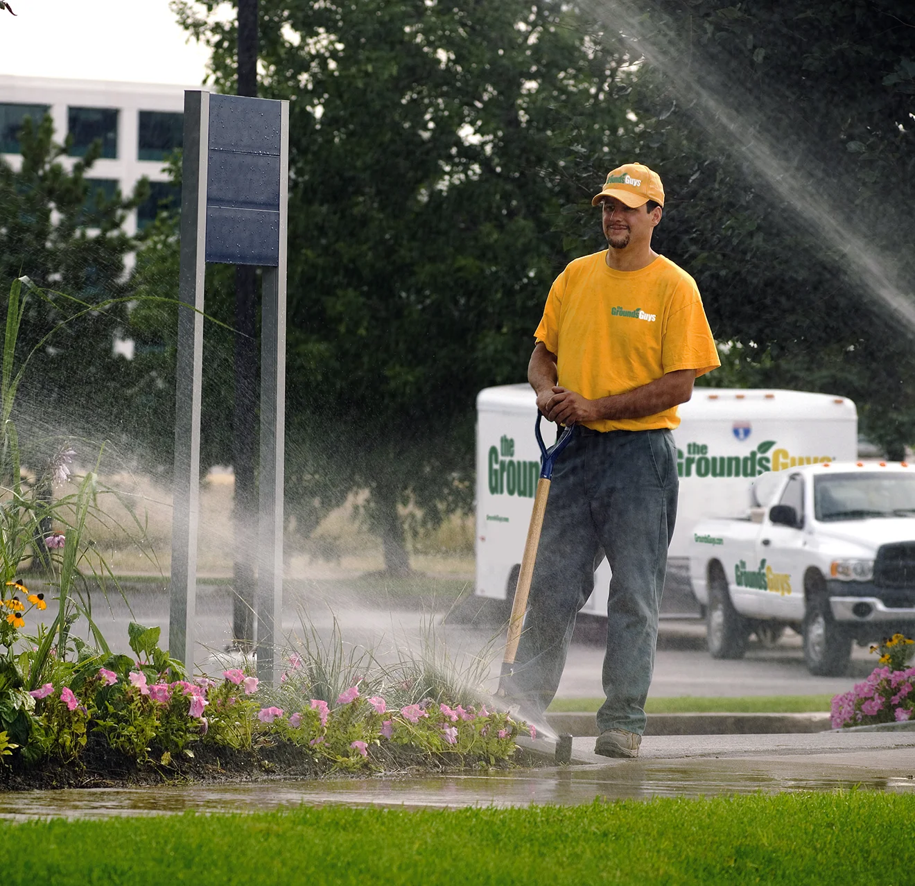 The Grounds Guys service professional monitoring sprinklers as they spray water on a lawn.