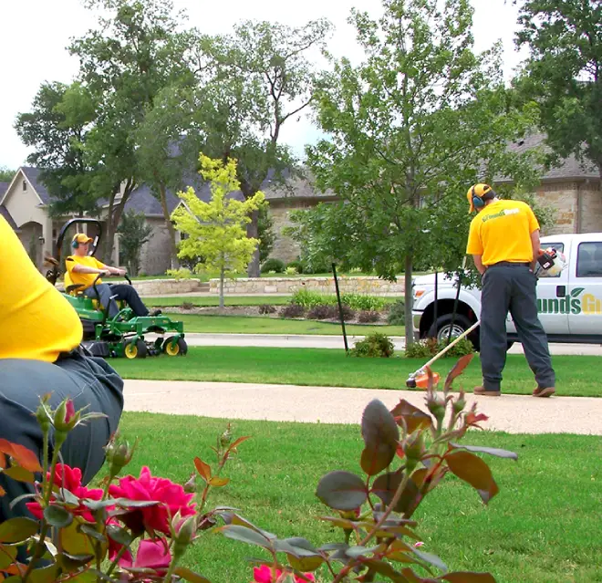 The Grounds Guys service professionals mowing and edging a front lawn.