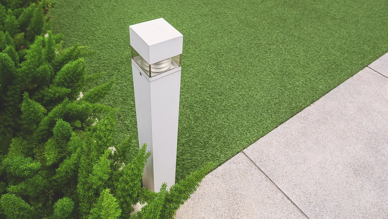 Artificial turf installed next to a stone walkway and a light column.