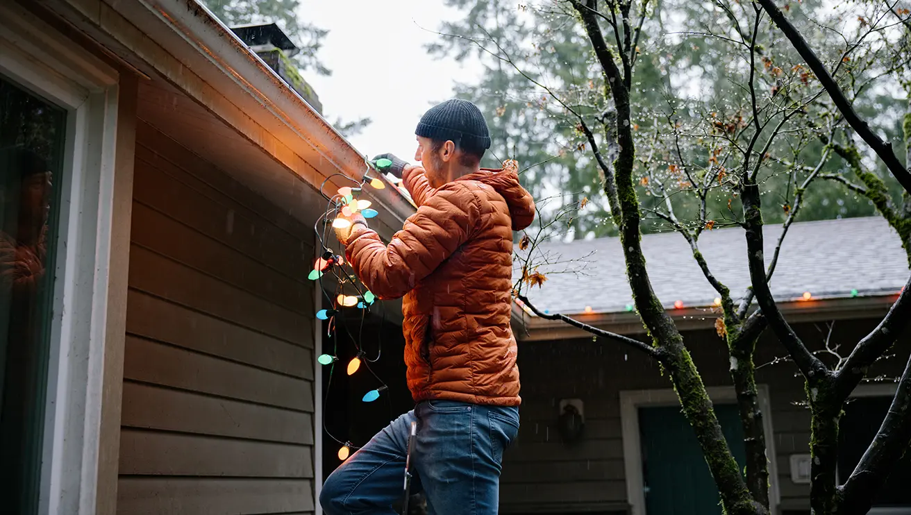 A large Colonial-style home with holiday lights and garland decorating the exterior.