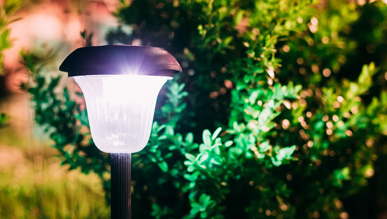 A solar-powered garden lantern emitting bright light next to a shrub.