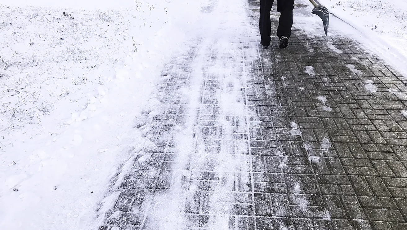 Snow cleared from a walkway, with a person's boots visible walking on path.