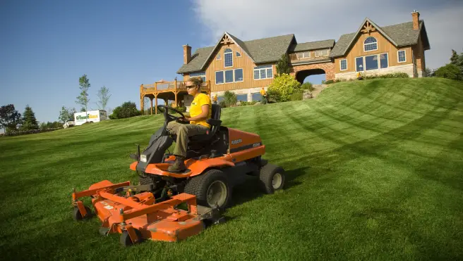 The Grounds Guys service professional mowing a large home's front lawn.