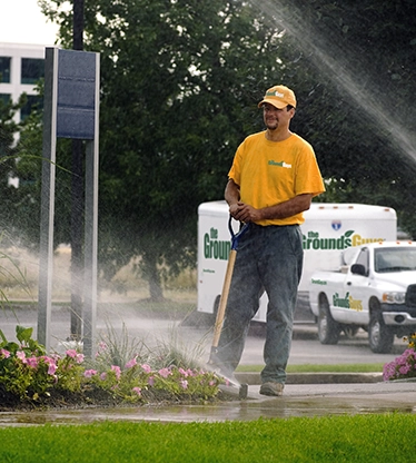 The Grounds Guys service professional monitoring sprinklers spraying water on a lawn.