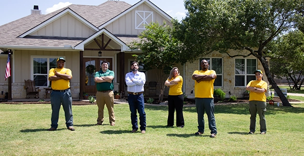 The Grounds Guys team standing with arms crossed in the front yard of a home.