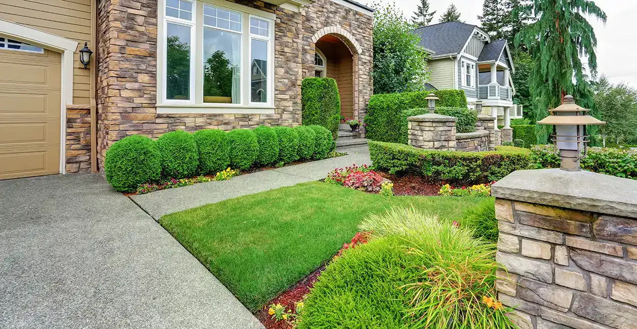 A home's front yard with trimmed shrubs, flowers, and low stone walls.