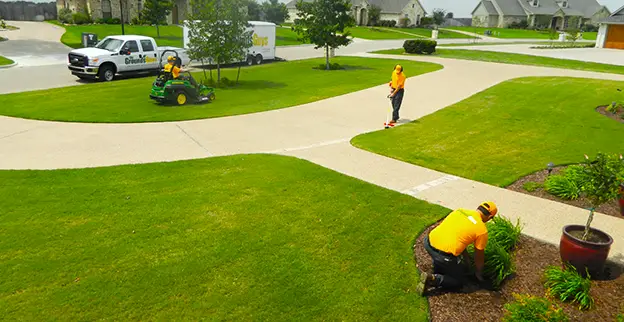 Three Grounds Guys service professionals mowing and edging a front lawn.