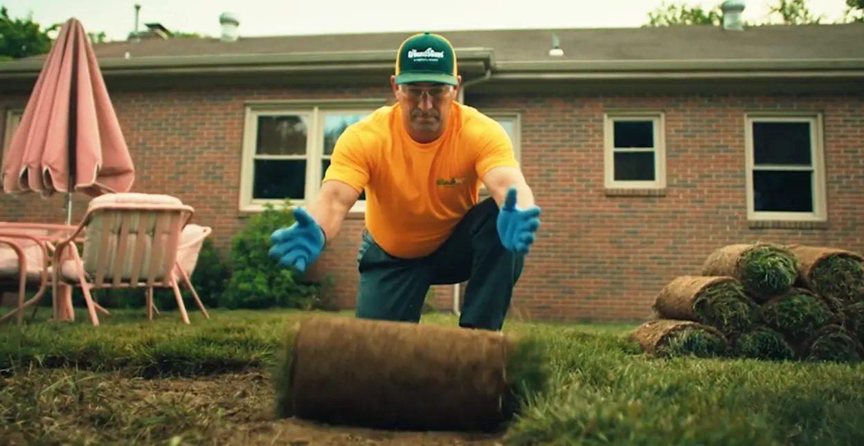 The Grounds Guys service professional unrolling a roll of sod in a backyard.