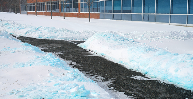 Snow cleared from the asphalt path outside a commercial building.