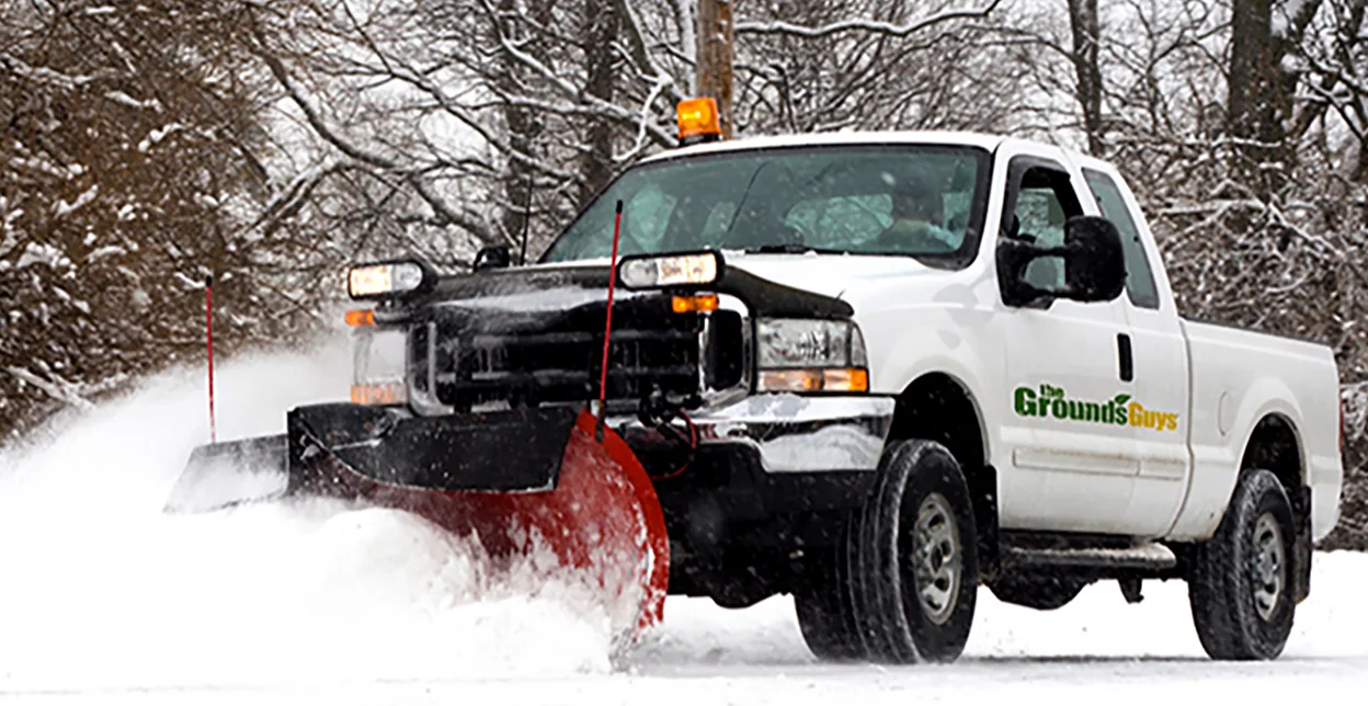 The Grounds Guys branded snow plow pushing snow off a road.