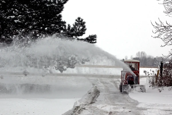 Lawn tractor with rotary snow blower plow being used to clear snow from driveway.