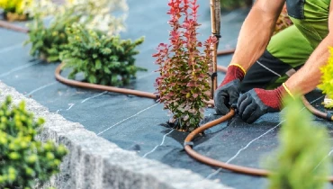 Man wearing gloves working on an irrigation system that is running through a garden.