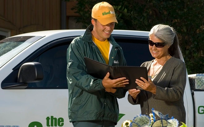 The Grounds Guys service professional reviewing a tablet with a client.