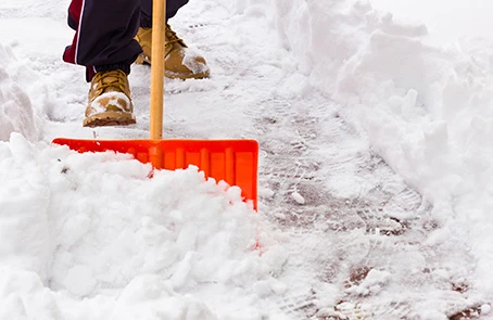 The Grounds Guys employee shoveling snow with red shovel.